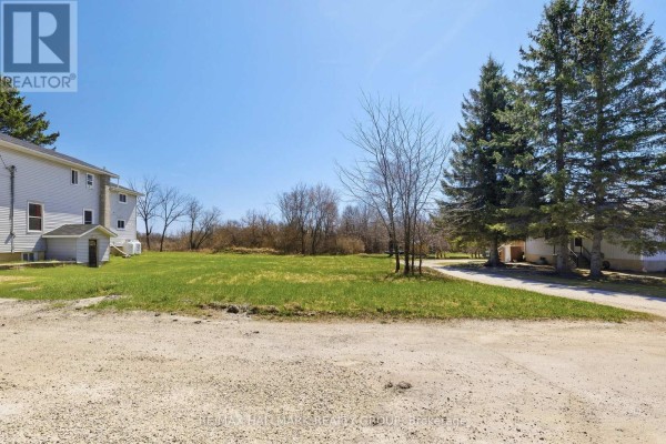 A wide view of a grassy lot with a light-grey house and trees under a bright blue sky. - 32 Brock Street N, Perth