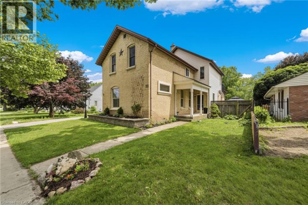 Side view of a yellow brick house with a porch and lawn. - 32 Clench Avenue, Brantford