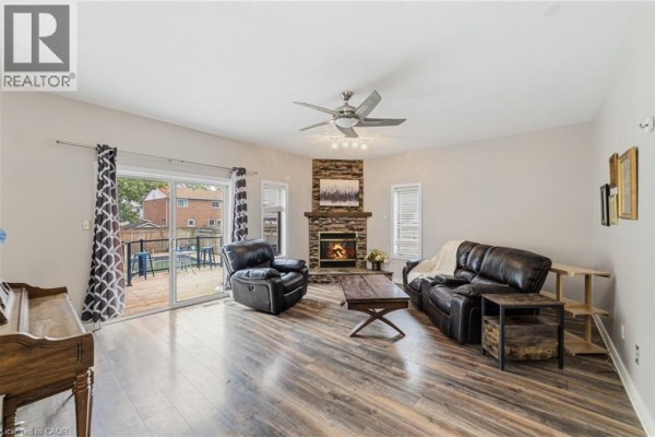 Living room with a stone fireplace, leather sofas, coffee table, and sliding glass doors. - 32 Clench Avenue, Brantford
