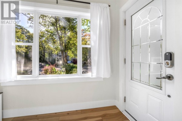 Interior entryway with a white door featuring glass panes, a large window with white curtains, and hardwood floors. - 32 Craigmillar Avenue, St  John S