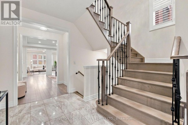 Hallway with a staircase featuring oak treads and black metal spindles, looking into a living room. - 32 Cyprus Glen, East Gwillimbury