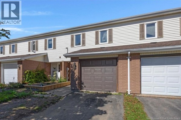 View of multiple townhouse units with beige siding, brick detailing, and driveways. - 32 Driftwood Lane, Saint John