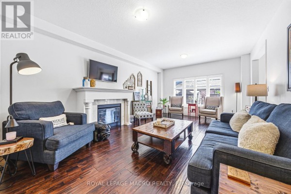 Living room with a fireplace, dark blue sofas, wooden floor, and large windows with white blinds. - 32 Dulgaren Street, Hamilton