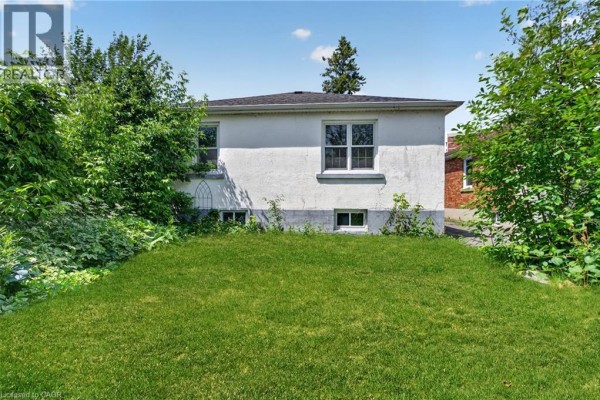 Rear exterior view of the bungalow showing a white stucco back wall and grassy backyard. - 32 Dunlop Street, Kingston