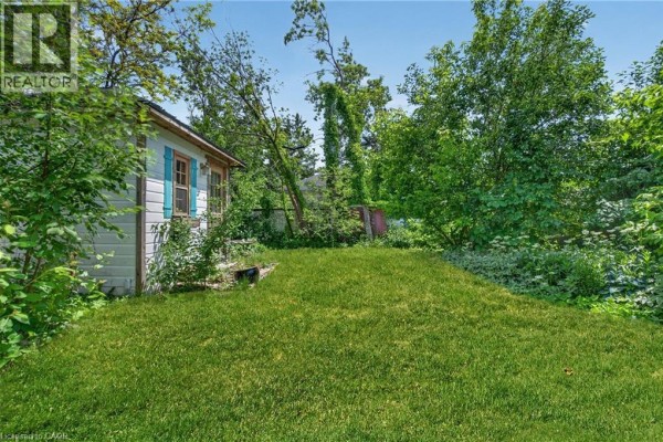 View of the backyard and side of the bungalow, featuring a grassy lawn and mature trees. - 32 Dunlop Street, Kingston