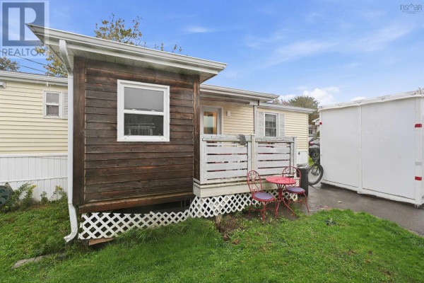 Back corner of the mobile home with a small wooden porch, two red chairs, and a white storage unit nearby. - 32 Earleton Avenue, Dartmouth