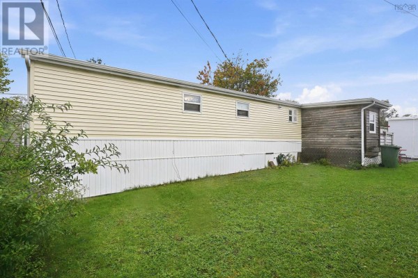 Long side view of the yellow mobile home with a green grassy lawn and a wooden fence. - 32 Earleton Avenue, Dartmouth