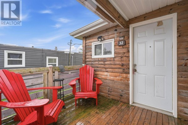 Close-up of the wooden porch with two red Adirondack chairs, a small table, and a white front door. - 32 Earleton Avenue, Dartmouth