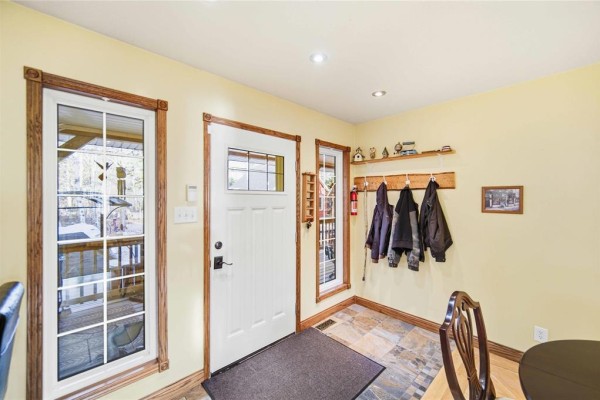 Interior entryway with yellow walls, white door, slate tile floor, and coats hanging on a rack. - 32 Eastshore Drive, Victoria Beach