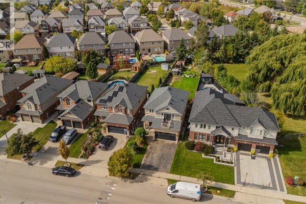 Aerial view of a suburban street with multiple two-story houses, manicured lawns, and mature trees. - 32 Great Oak Trail, Binbrook