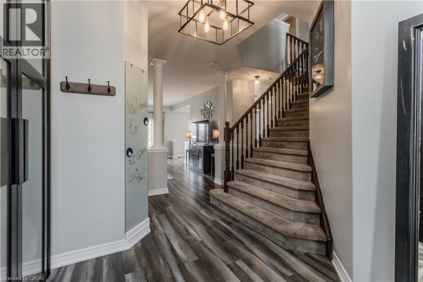 Interior entryway with grey laminate flooring, a carpeted staircase with a dark wood banister, and decorative columns. - 32 Great Oak Trail, Binbrook