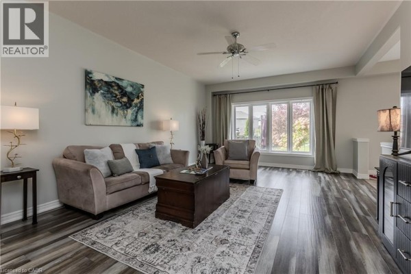 Living room with a beige sofa, armchair, dark wood coffee table, patterned rug, and a large window with curtains. - 32 Great Oak Trail, Binbrook