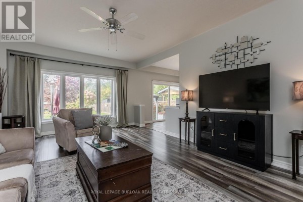 Living room with a sofa, armchair, coffee table, television, and a view of the backyard. - 32 Great Oak Trail, Hamilton