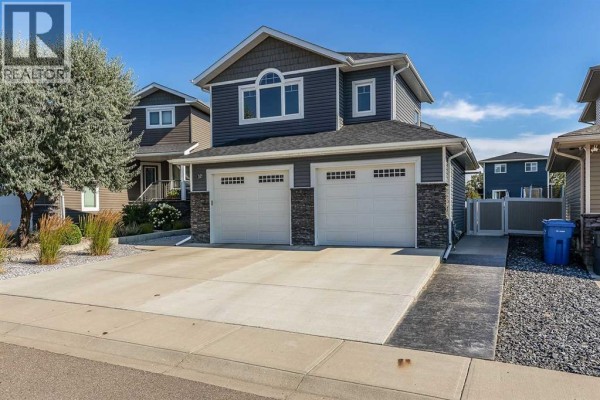 Side exterior view of a dark blue two-story house with a double garage and stone accents. - 32 Hamptons Crescent Se, Medicine Hat