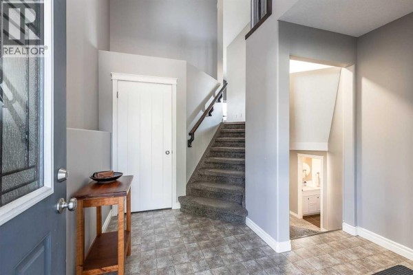 Interior entryway with a staircase, white door, tile floor, and a small wooden table. - 32 Hamptons Crescent Se, Medicine Hat