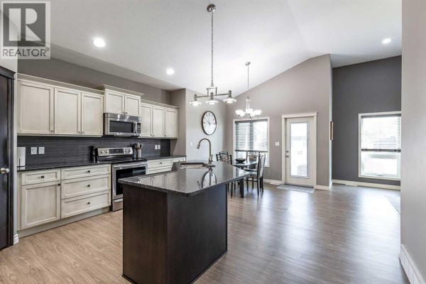 Modern kitchen and dining area with vaulted ceiling, island, stainless steel appliances, and dark grey accent wall. - 32 Hamptons Crescent Se, Medicine Hat