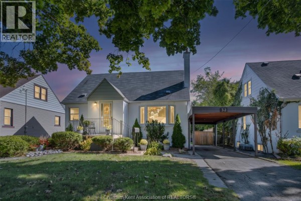 Evening twilight view of the white house with illuminated windows, carport, and shadowy trees. - 32 Kerr Avenue, Chatham
