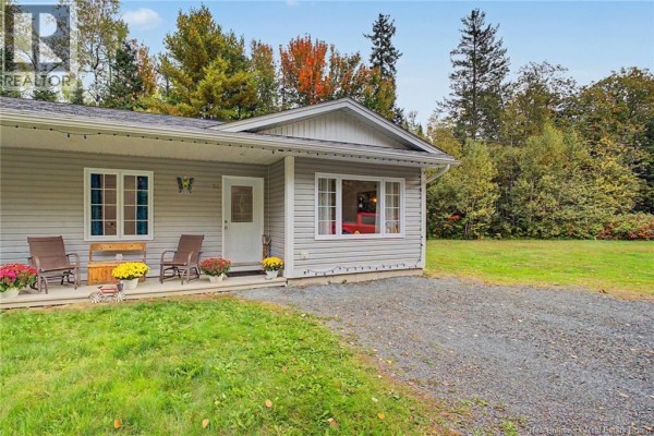 Front view of a grey garden home with a covered porch, entryway, and surrounding trees. - 32 Lena's Woods Lane, Geary