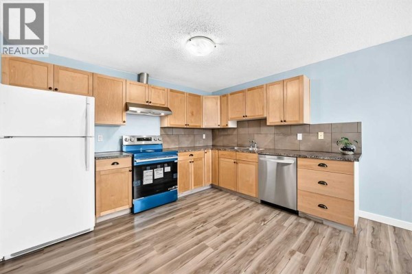 L-shaped kitchen with light wood cabinets, granite countertops, stainless steel appliances, and light blue walls. - 32 Macewan Park Link Nw, Calgary