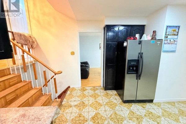 Hallway with a staircase, stainless steel refrigerator, and dark wooden cabinets. - 32 Madison Street, Brampton