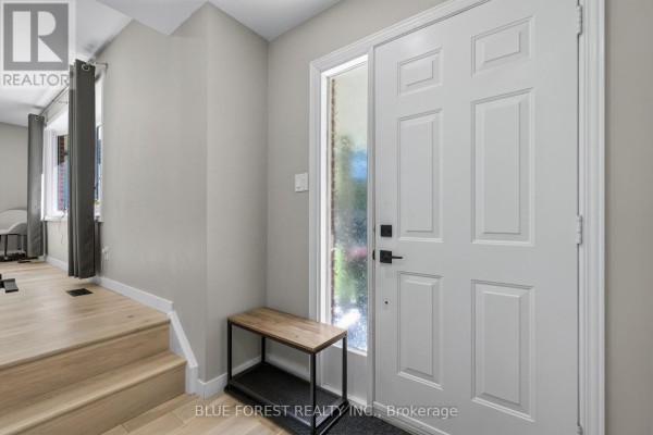 Interior view of a bright white front entryway with a large door, sidelight window, and a wooden bench. - 32 Meadowview Road, London South