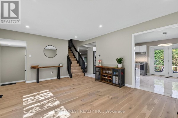 Spacious living area with light wood flooring, grey walls, a staircase, and an open view to the kitchen and backyard. - 32 Meadowview Road, London South