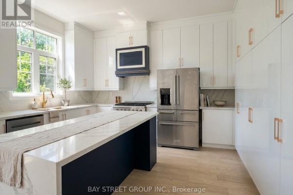 Modern white kitchen with a large island, stainless steel appliances, and marble countertops. - 32 Moreau Way, Springwater