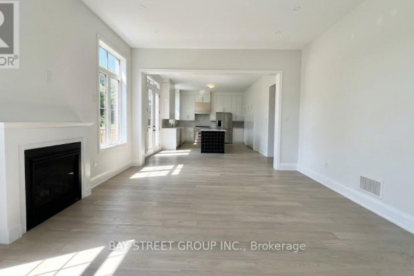 Living room with a gas fireplace and view into a white modern kitchen with an island. - 32 Moreau Way, Springwater