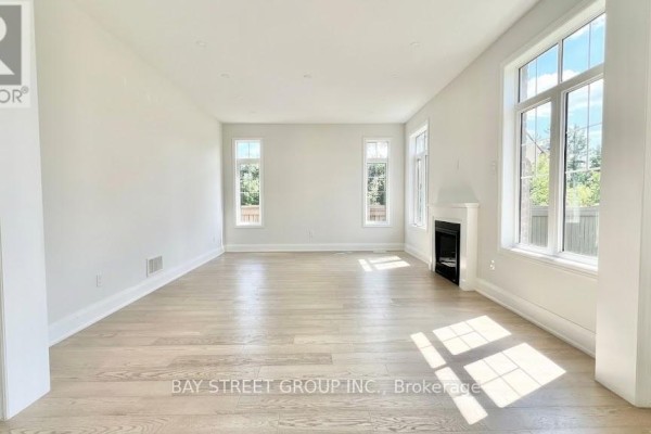 Spacious living room with a fireplace, hardwood floors, and large windows overlooking greenery. - 32 Moreau Way, Springwater
