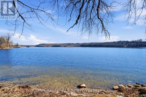 Waterfront view of a calm lake with trees and shoreline - 32 Quinte View Road Greater Napanee
