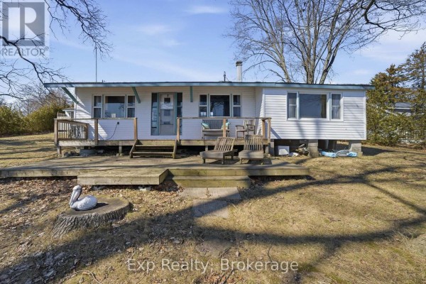 Outdoor view of a lake and trees from a wooden deck with a boathouse and dock visible. - 32 Quinte View Road, Greater Napanee