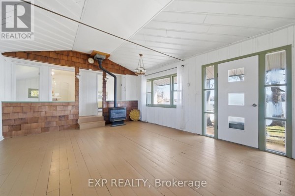 Living room with wood stove, paneled walls & ceiling, and large windows - 32 Quinte View Road Greater Napanee
