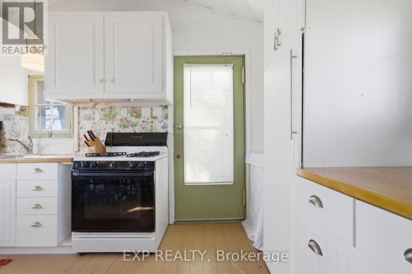 White cabinets, gas range, and floral wallpaper in kitchen - 32 Quinte View Road Greater Napanee