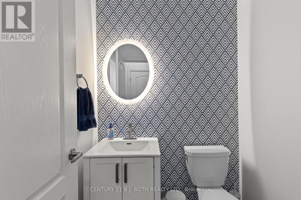 Powder room with a white vanity, sink, oval mirror, and geometric wallpaper. - 32 Sandhill Crane Drive, Wasaga Beach