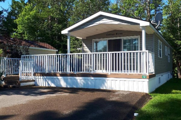Front view of a grey mobile home with a white deck, white railings, and a covered entrance. - 32 Temagami Trail, Wasaga Beach