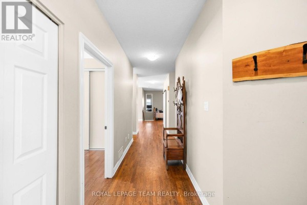 Long hallway with hardwood floors, white doors, and a wooden coat rack. - 32 Trump Avenue, Ottawa