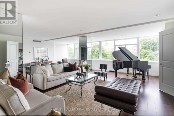 Open-concept living area with a grand piano, seating areas, and large windows overlooking greenery. - 320 - 1 Benvenuto Place, Toronto