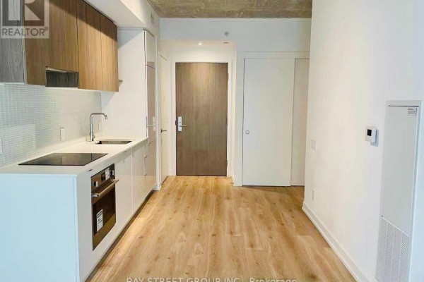 Compact kitchen area with light wood floors, white cabinetry, stainless steel appliances, and a wood-paneled accent wall. - 320 - 161 Roehampton Avenue, Toronto