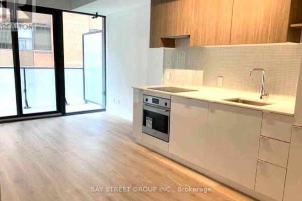 Kitchen area with white countertops and cabinets, stainless steel appliances, and glass doors leading to a balcony. - 320 - 161 Roehampton Avenue, Toronto
