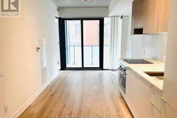 View of a modern condo interior with light wood floors, white walls, and sliding glass doors to a balcony. - 320 - 161 Roehampton Avenue, Toronto