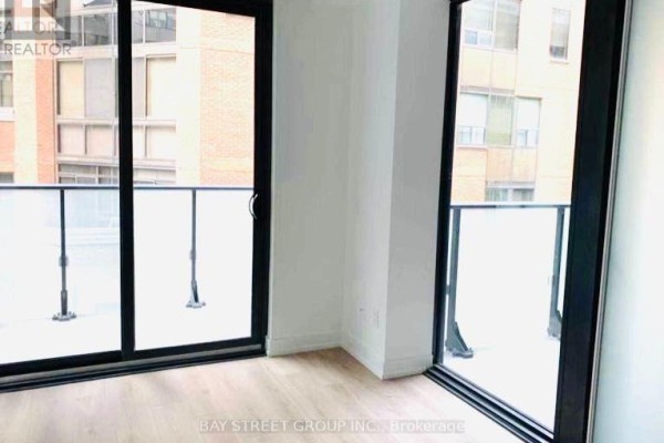 Interior view showing two sliding glass doors with balcony access and city building views beyond. - 320 - 161 Roehampton Avenue, Toronto