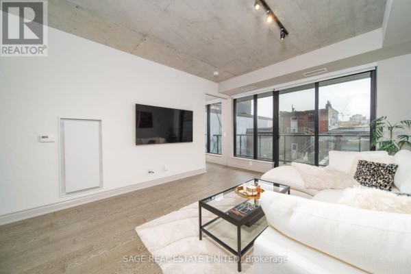 Living room with a white sofa facing a television and large windows overlooking the city. - 320 - 608 Richmond Street W, Toronto