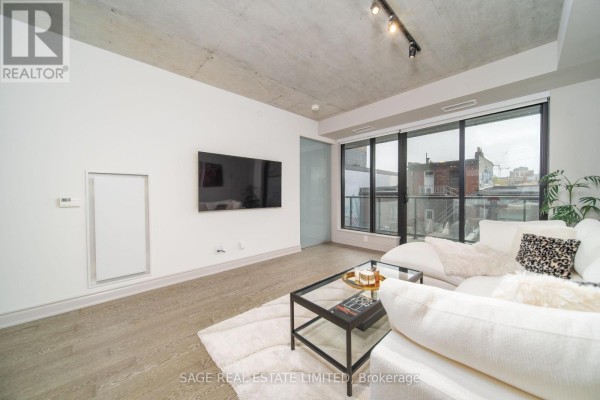 Living room with a television on the wall and large windows with city views. - 320 - 608 Richmond Street W, Toronto