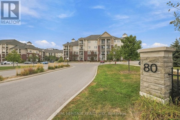A stone pillar with '80' on it next to a paved road leading to apartment buildings. - 320 - 80 Aspen Springs Drive, Clarington
