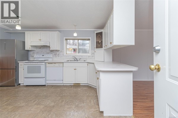 Open kitchen with white cabinets, stainless steel appliances, and light-colored countertops - 320 2885 Boys Rd, Duncan