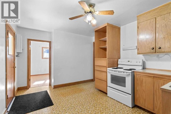 Kitchen with white appliances, light wood cabinets, and a patterned yellow floor, viewed from the entrance. - 320 4 Avenue S, Three Hills