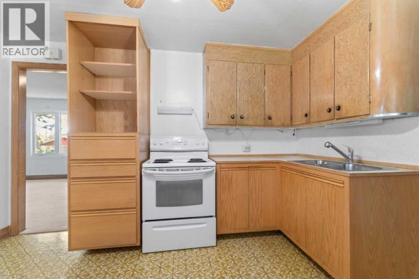Kitchen with white appliances, light wood cabinets, and a patterned yellow floor, showing the sink and counter. - 320 4 Avenue S, Three Hills