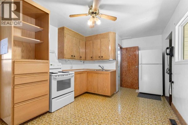 Kitchen with white appliances, light wood cabinets, a patterned yellow floor, and a white refrigerator on the right. - 320 4 Avenue S, Three Hills