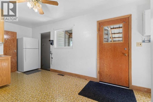 Kitchen with a white refrigerator, a patterned yellow floor, a small window, and a wooden door on the right. - 320 4 Avenue S, Three Hills
