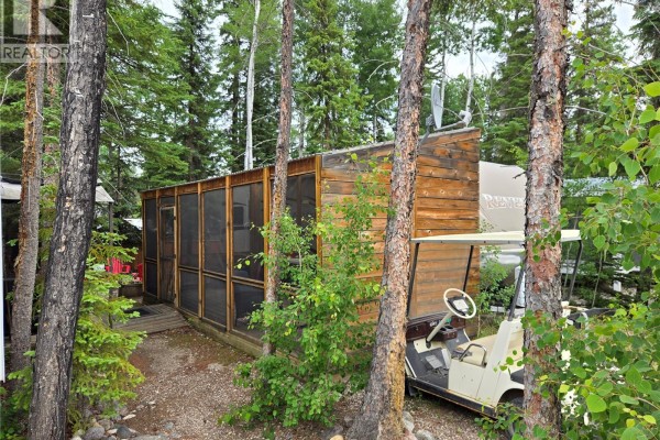 Side view of a wooden shed with a screened-in porch and a golf cart. - 320 Fairway Drive, Candle Lake